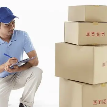 A professional packer taking notes next to a stack of packed boxes