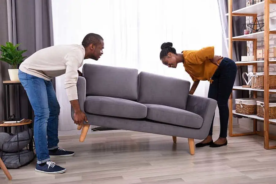 Woman holding her back while trying to lift a heavy couch with her husband