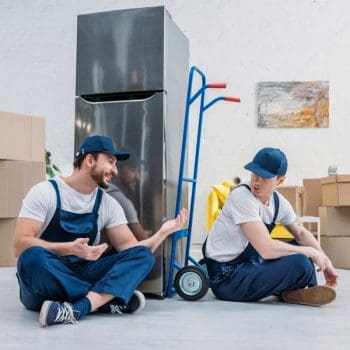 Two professional movers with a large appliance dolly