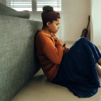 Woman sitting on a bedroom floor with a contemplative look