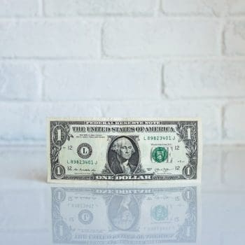 Dollar bill posed standing up on its own against white brick backround
