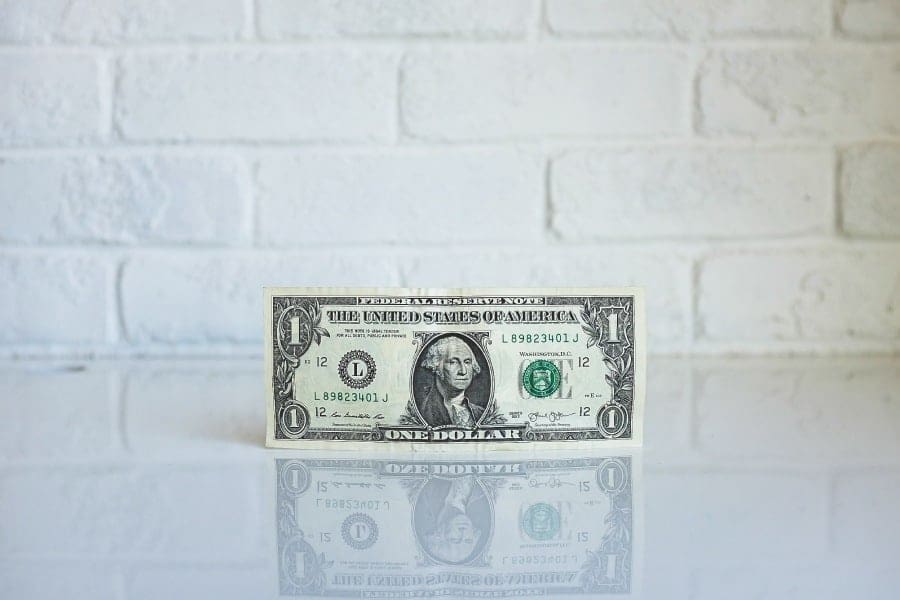 Dollar bill posed standing up on its own against white brick backround