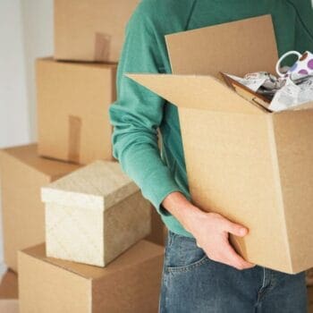 Man holding a moving box filled with ceramic mugs and other kitchen items
