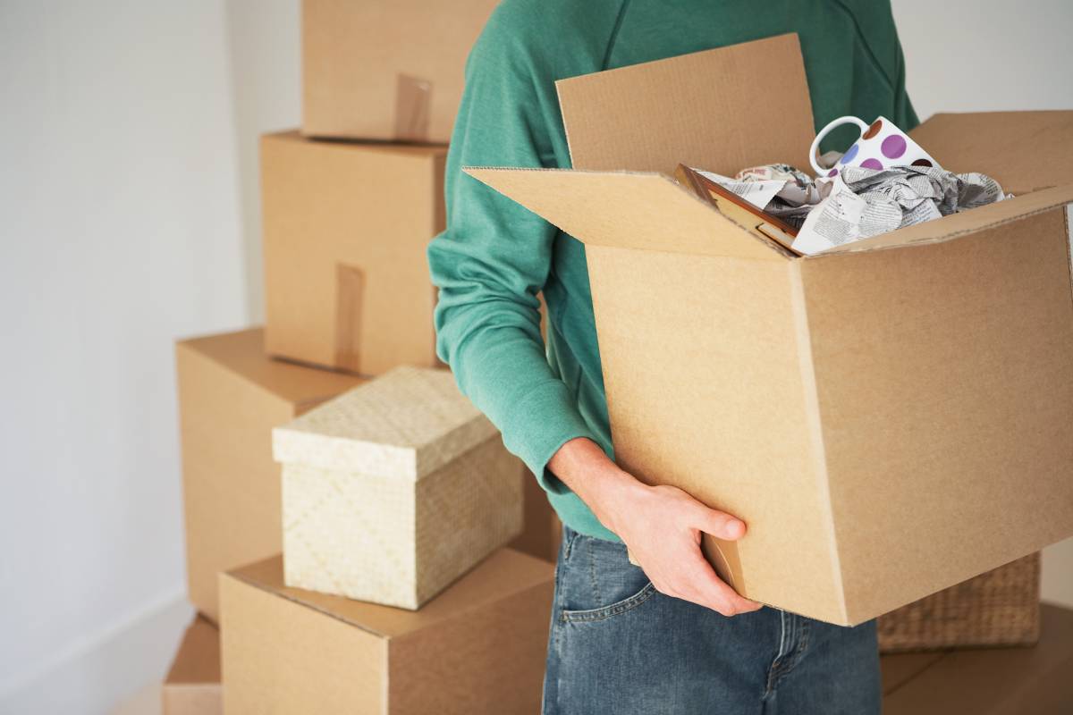 Man holding a moving box filled with ceramic mugs and other kitchen items